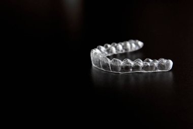 Şeffaf görünmez ortodonti, diş hizalayıcılar, plastik diş telleri, ağız koruyucular, siyah arka planda diş koruyucuları. 