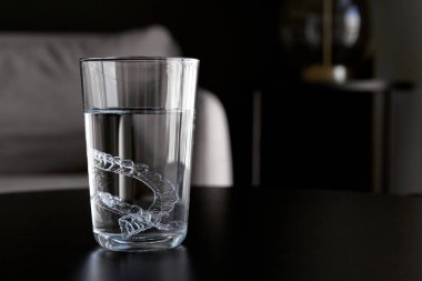 Şeffaf görünmez ortodontik diş hizalayıcılar, dairedeki bir masada suyla bardakları temizleyen diş koruyucular.