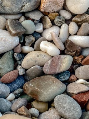Sahildeki renkli pürüzsüz çakıl taşlarının yüksek çözünürlüklü makro fotoğrafı. Detaylı dokuları ve toprak tonlarıyla doğal yuvarlak taşlar. Arkaplan, doğa projeleri veya tasarım kullanımı için ideal.