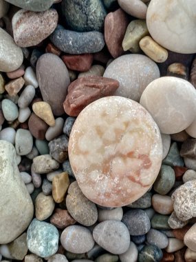 Merkezinde pürüzsüz ve dokulu doğal tonlarda taşlarla çevrili büyük yuvarlak pembe taşlı kumsal çakıl taşlarının Macro fotoğrafı. Doğa, jeoloji ve dokuya bağlı tasarımlar için ideal.