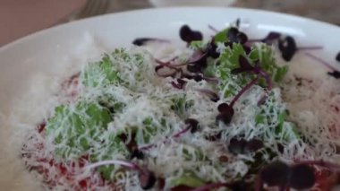 Parmesan peyniri ile süslenmiş çiğ et yemeği ve iştah açıcı bir restoranda yapraklar.