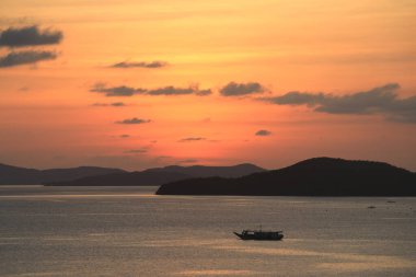 Filipinler, Busuanga adasındaki dağların arka planında büyüleyici bir alacakaranlık. Bir balıkçı eve dönerken görüldü. Suyun üzerinde güzel bir yolculuk izi bırakıyordu..