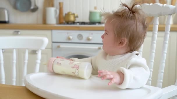自宅のキッチンでボトルから牛乳を動力を飲んでいる間に泣いてかわいい乱雑な赤ちゃんの女の子 母親は子供を落ち着かせる 子供の液体食品 人工または母乳栄養の概念 — ストック動画