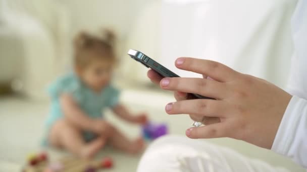 妈妈带着孩子在家里用手机 网上购物 社交媒体 在家里工作 而孩子们在玩耍 妇女寻找养育子女的信息 应用于父母 日常生活中的技术 — 图库视频影像