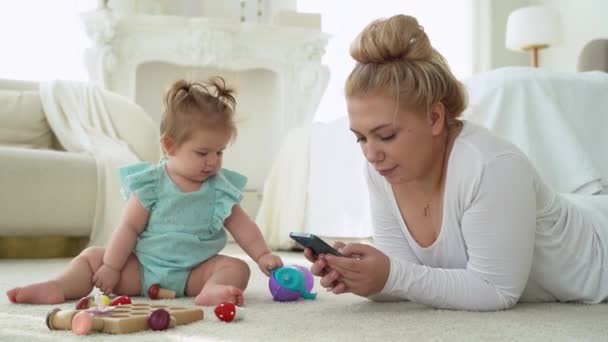 Νεαρή Μητέρα Ψωνίζει Online Χρησιμοποιώντας Smartphone Ενώ Παίζει Μωρό Γυναικεία — Αρχείο Βίντεο