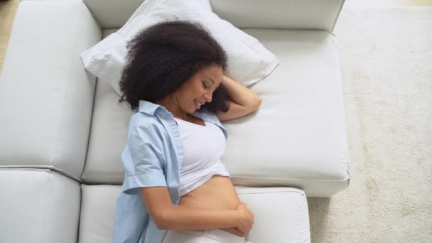 怀孕的黑人美女躺在家里的沙发上 摸着肚子 梦想着未来 有意识怀孕的轻松和健康的概念 — 图库视频影像