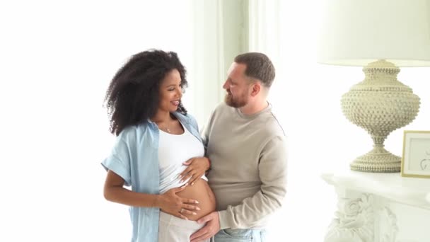 白い男が妊娠中の黒い妻の腹に触れた 妊娠中の女性と愛する夫は家でおなかを抱いています 妊娠中の腹の上の多民族カップルによる赤ちゃんの動きを感じ — ストック動画