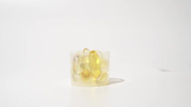 Kadın eli, beyaz arka plan üzerinden şeffaf altın hapları ölçme kabına koyar.