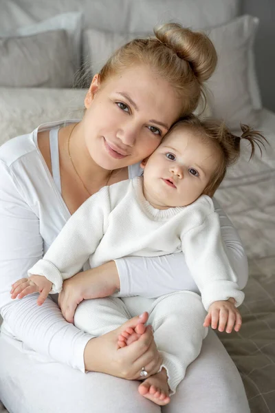 Portrait of young tired Mother and baby girl looking at camera in bedroom home. Child care, domestic life routine, healthy lifestyle. Exhausted woman take care about child and household duties. Copy space, vertical