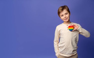 Cute caucasian boy child elementary school hold rainbow heart over purple blue background banner. Health insurance, donation charity, world heart day, appreciation, world children day, think positive clipart