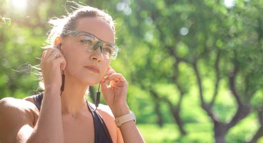 Close up Sport woman sportswear and headphones tie laces while training jogging running outside in green park banner, copy space for design.