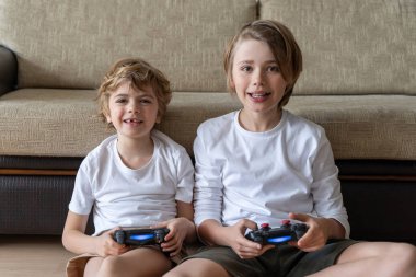 Funny caucasian siblings are relaxing together, playing video games in front of tv, two brother sister expressing emotions while enjoying their hobby playstation joystick