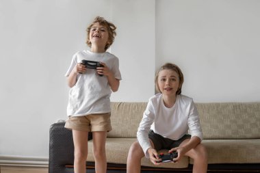 Funny caucasian siblings passionately playing video games in front of tv, two brother sister expressing emotions while enjoying their hobby joystick. Copy space