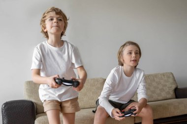 Funny caucasian siblings passionately playing video games in front of tv, two brother sister expressing emotions while enjoying their hobby playstation joystick. Copy space