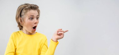 Impressed Emotional School boy happily Joy Showing To Right Over White Background. Copy Space For Advertisement. Excited Blond Kid With Long Hair And Yellow T-Shirt