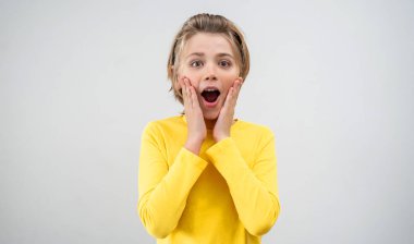 Amazed School boy happily Joy Looking At Camera Over White Background. Copy Space For Advertisement. Excited Blond Kid With Long Hair And Yellow T-Shirt