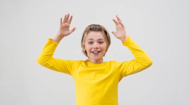 Cheerful Emotional School Boy happily Waving hands up Over White Background. Blond Kid With Long Hair And Yellow T-Shirt Waving Hands Excited. Copy space