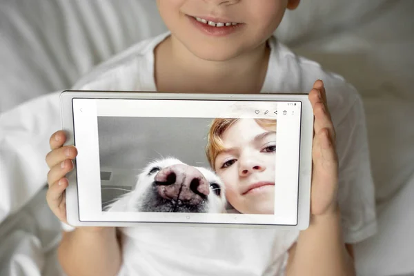 Child girl showing selfie with favorite pet dog on digital screen of tablet. Happy childhood with pets.