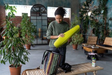 Beautiful multiethnic woman with packing her stuff after sport training in fitness class. Lifestyle wellbeing.