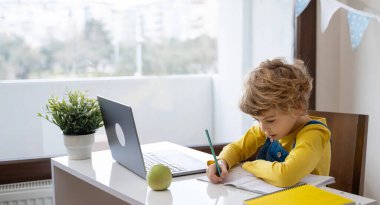 Caucasian child schoolboy or girl studying at home using laptop remote education. Doing homework, writing exercise book. Copy space