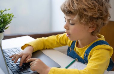 Close-up of child hands typing on the keyboard laptop. Distance learning online education. Schoolboy girl studying at home with digital tablet notebook and doing school homework. Side view