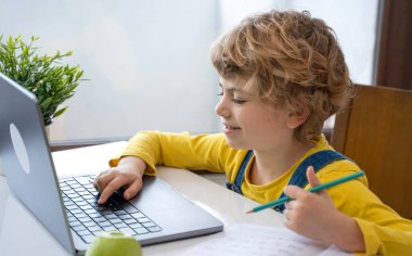 Close-up of child hands typing on the keyboard laptop. Distance learning online education. Schoolboy girl studying at home with digital tablet notebook and doing school homework. Side view