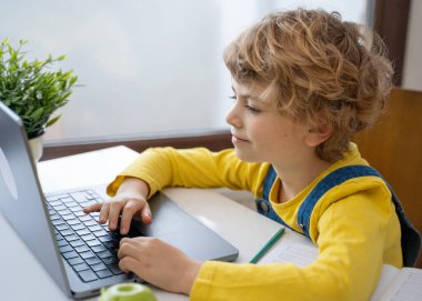 Close-up of child hands typing on the keyboard laptop. Distance learning online education. Schoolboy girl studying at home with digital tablet notebook and doing school homework. Side view