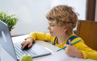 Close-up of child hands typing on the keyboard laptop. Distance learning online education. Schoolboy girl studying at home with digital tablet notebook and doing school homework. Side view