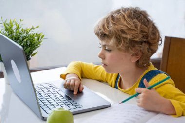 Close-up of child hands typing on the keyboard laptop. Distance learning online education. Schoolboy girl studying at home with digital tablet notebook and doing school homework. Side view