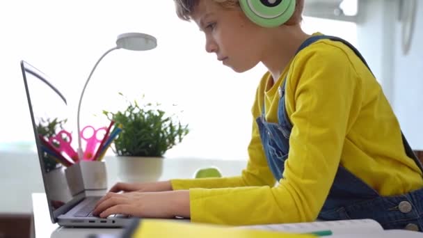 かわいいスマート白人小学校キーボードのラップトップに入力するヘッドフォンを持つ子供 家庭でデジタルクラス コンピュータ上のWebレッスンを教えるオンライン家庭教師 バーチャル教育 女子高生 — ストック動画