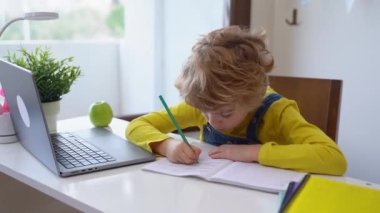 Okullu çocuk evde dizüstü bilgisayarla eğitim programlama kursunu kullanarak egzersiz alfabesi yazıyor. Uzaktan kumandalı video konferansı. Öğrenci kız çalışması ev ödevi yapıyor..