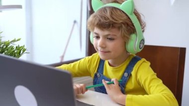 Cute smart caucasian primary School Child with headphones educate online laptop. Tutor teaching digital class, web lesson on computer at home. Virtual education course. Schoolboy girl studying doing