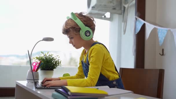 可爱的聪明的高加索小学生 带着耳机在键盘上打字 网上家教数字化课程 网上家教电脑 虚拟教育 在校女生在学习 — 图库视频影像