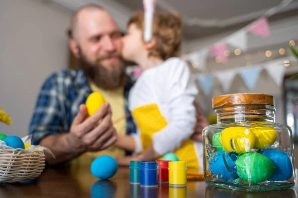 Easter Family traditions. Father and caucasian happy child with bunny ears dye and decorate eggs with paints for holidays while sitting together at home table having fun. Copy space