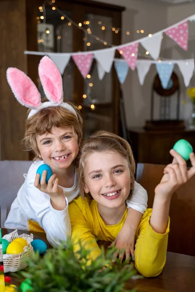 Easter Family traditions. Two caucasian happy children with bunny ears dye and decorate eggs with paints for holidays playing together. Kids having fun. Vertical