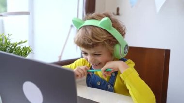 Cute smart caucasian primary School Child with headphones educate online laptop. Tutor teaching digital class, web lesson on computer at home. Virtual education course. Schoolboy girl studying doing