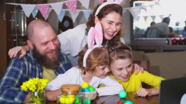 Happy family Easter tradition. Remote greeting relatives using laptop, painting egg, bunny ears. Christian religious holiday Sunday togetherness