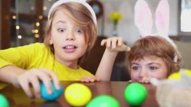 Mutlu Paskalyalar. Komik çocuklar evde renkli yumurtalarla oyun oynarlar. Tatlı çocuklar paskalya tavşanı avcılarını oynuyor.