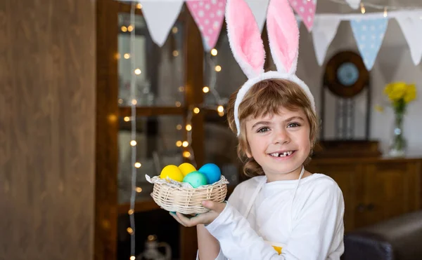 Easter Family traditions. Caucasian happy child with bunny ears posing with wicker decorate eggs looking at camera.