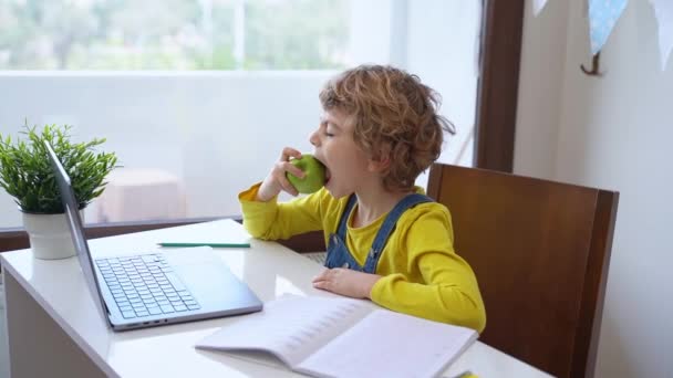 可爱的学童一边吃苹果 一边在家里用笔记本电脑上教育课 远程学习课程远程视频会议 女学生的学习做家庭作业 — 图库视频影像