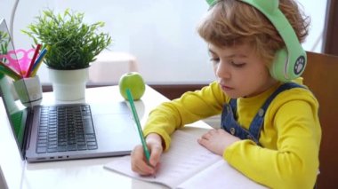 Laptop kullanan kulaklıklı şirin, zeki, beyaz bir ilkokul çocuğu. Çevrimiçi öğretmenlik, dijital dersler, evde bilgisayar dersleri. Sanal eğitim. Öğrenci kız ders çalışıp ödev yapıyor.