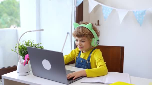 可愛いスマート白人小学校ヘッドフォンで子供はオンラインノートパソコンを教育します 家庭でデジタルクラスやWebレッスンを教えています バーチャル教育コース 勉強してる女子高生 — ストック動画