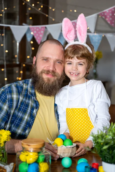 Easter Family traditions. Father and caucasian happy child with bunny ears dye and decorate eggs with paints for holidays while embrace together at home table. Vertical