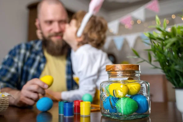 Easter Family traditions. Father and caucasian happy child with bunny ears dye and decorate eggs with paints for holidays while sitting together at home table having fun. Negative space