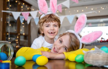 Easter Family traditions. Two caucasian happy children bunny ears playing with decorated multi-colored eggs. Kid having fun looking at camera. Negative copy space. Selective focus