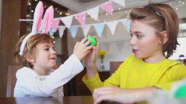 Easter Sunday Family holiday traditions. Two caucasian happy siblings kids with bunny ears fighting with multi-colored Easter painted eggs. Having fun together