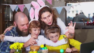 Happy family Easter tradition. Remote greeting relatives using laptop, painting egg, bunny ears. Christian religious holiday Sunday togetherness