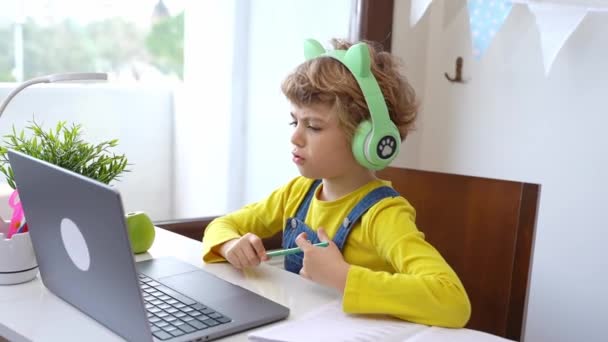 可愛いスマート白人小学校ヘッドフォンで子供はオンラインノートパソコンを教育します 家庭でデジタルクラスやWebレッスンを教えています バーチャル教育 宿題を勉強する女子高生 — ストック動画