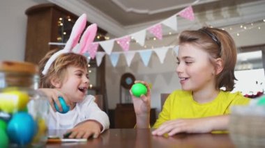 Easter Sunday Family holiday traditions. Two caucasian happy siblings kids with bunny ears fighting with multi-colored Easter painted eggs. Having fun together