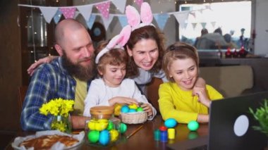 Happy family Easter tradition. Remote greeting relatives using laptop, painting egg, bunny ears. Christian religious holiday Sunday togetherness